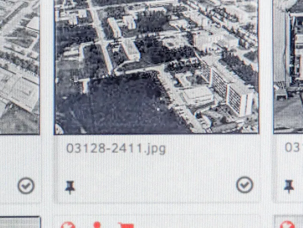 A pixelated screenshot of an interface, focused on an image, which is partially out of the frame, whose name is "03128-2411.jpg". Under the name, there is the logo of a pin in a rounded, checked box. The image is quite blurry, but it seems like an aerial picture of a complex with some buildings.
